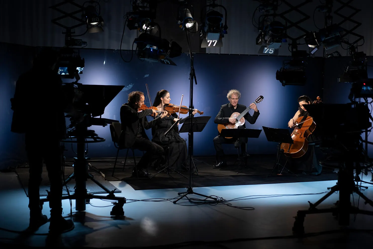 The ensemble recording in a television studio, seated among cameras and stage lights