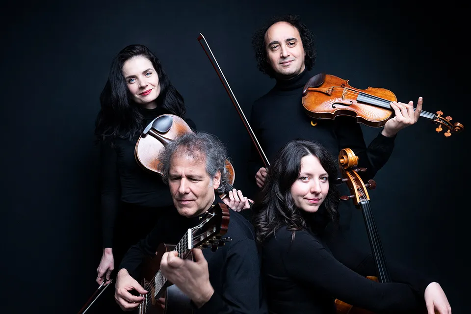 Close group portrait: violist and violinist standing, guitarist and cellist seated in front, all smiling at the camera