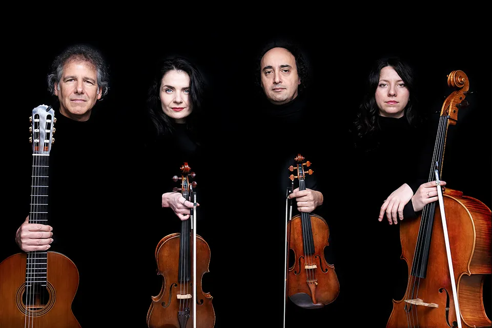 The four musicians standing in a row holding guitar, viola, violin and cello upright in front of them