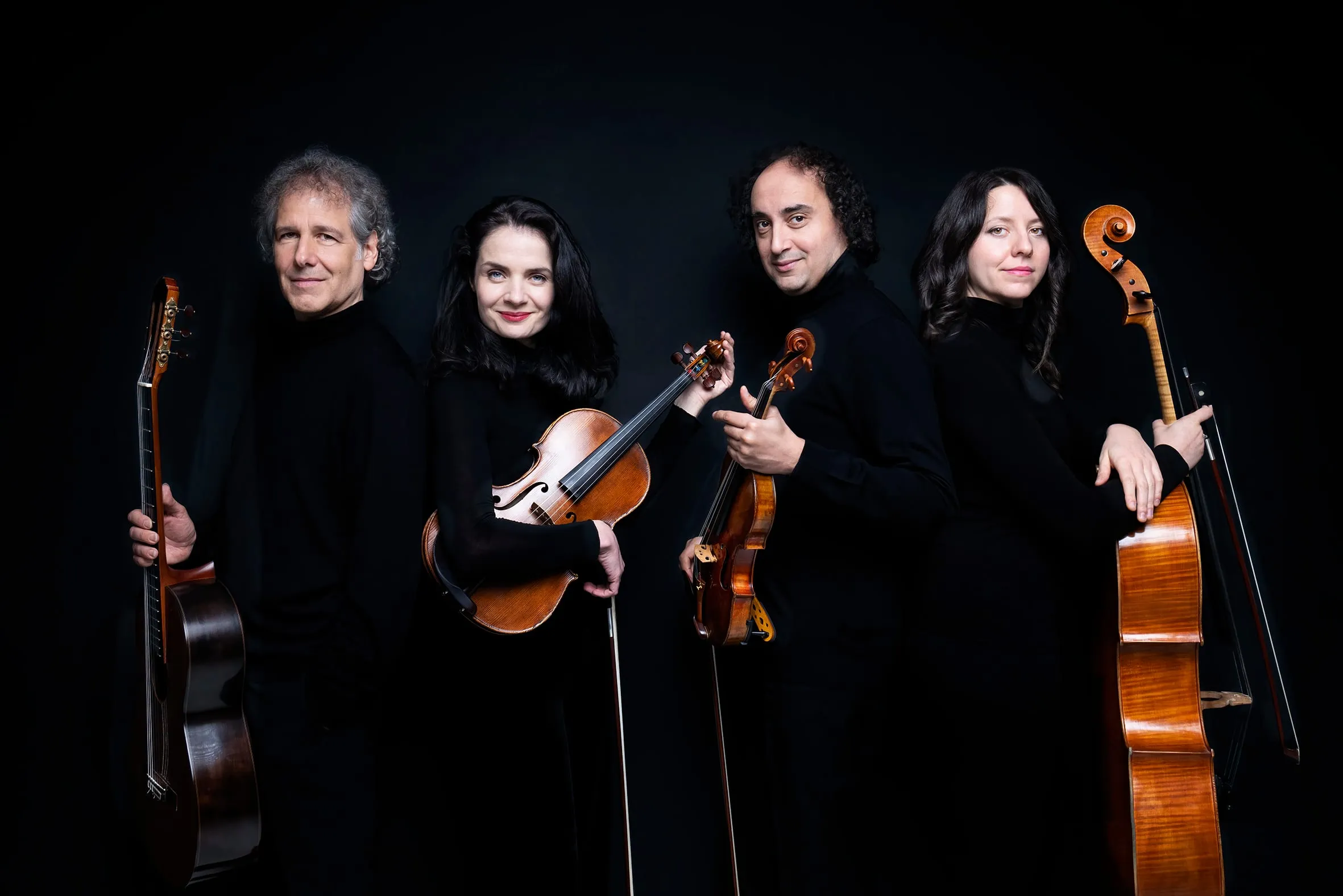 The four musicians standing close together at an angle, instruments held across their bodies